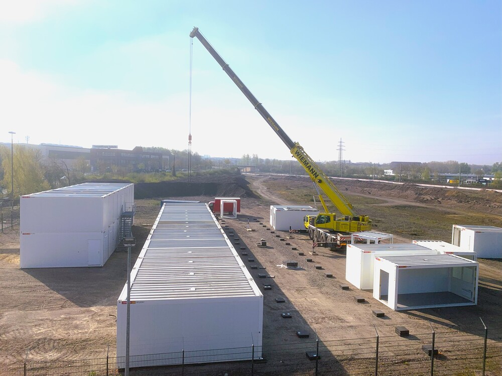 Blick auf das Containerdorf: Noch befindet sich das Containerdorf im Aufbau, einige Container fehlen noch. Ein großer Kran, hebt die Container an die richtige Stelle.
